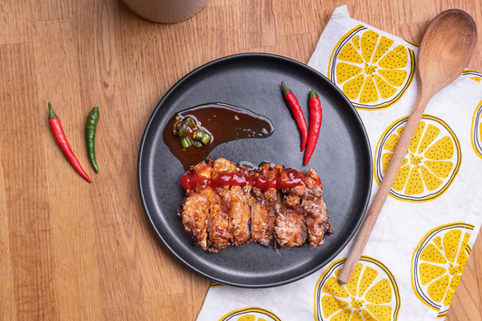 Crispy sweet chili chicken thighs drizzled with Yeo's Sweet Chili Sauce and lime glaze on a white plate