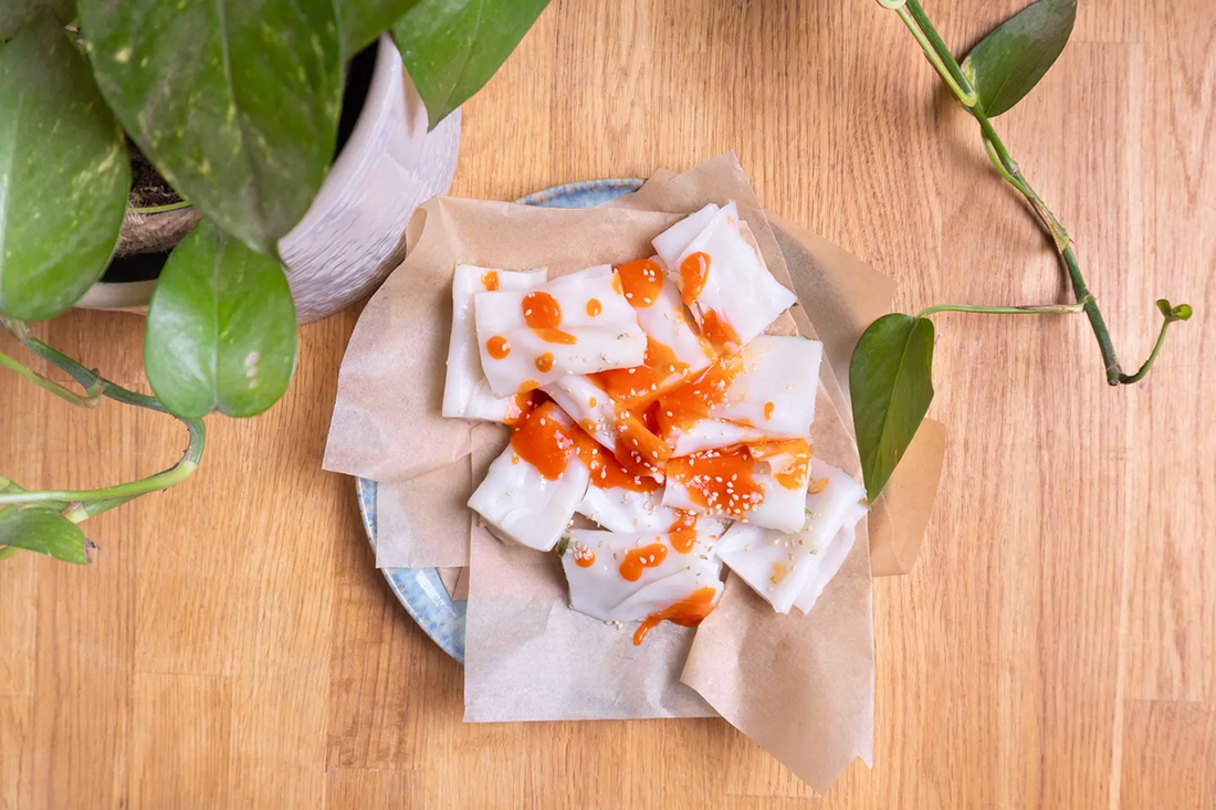 Hong Kong style cheung fun rice noodle rolls drizzled with Yeo's Chili Garlic Sauce and sesame seeds on a white plate