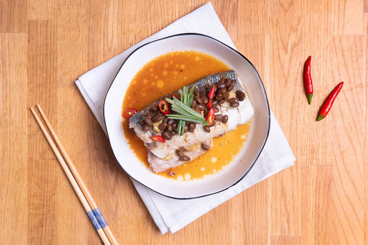 Cantonese steamed fish topped with Yeo's Salted Soybeans, shredded green onions, and red chili on a white plate